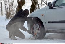 Un homme en train de mettre des chaînes à neige. 