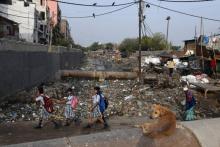 Des écolières passent devant un canal d'évacuation des égoûts rempli de déchets dans le bidonville Taimur Nagar à New Delhi le 30 mai 2018