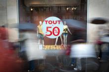 Des piétons passent devant une vitrine avec un autocollant "Tout à -50%", au premier jour des soldes d'été à Paris, le 22 juin 2011